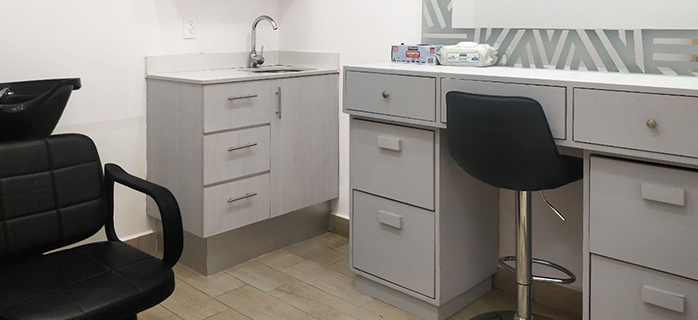 This image shows a clean and organized room designed for head washing and shaving prior to a hair transplant procedure. It features a sink with cabinets, a comfortable black chair, and a workstation with drawers and a barstool, creating a professional and functional environment. The design emphasizes practicality and hygiene in preparation for the procedure.