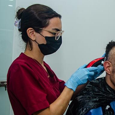 A female doctor in a red uniform is trimming the donor area with precision, preparing for a hair transplant procedure