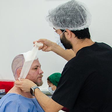 A medical professional in a black uniform carefully applying a bandage to a patient’s head after a hair transplant procedure