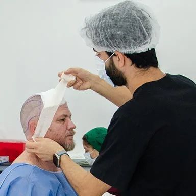 A medical professional in a black uniform carefully applying a bandage to a patient’s head after a hair transplant procedure